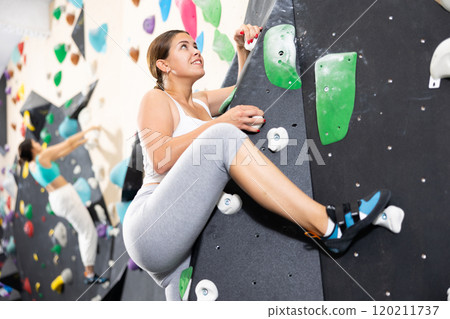 Young Europian woman climbs steep artificial wall in sports complex and trains endurance 120211737