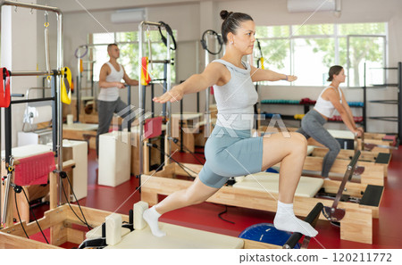 Sportive young girl training her arms and legs on reformer device 120211772