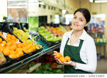 Young woman in uniform sells tangerines in grocery store Young woman in uniform sells tangerines in grocery store 120211807
