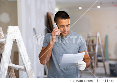 Man with documents talking on phone in building site 120211838