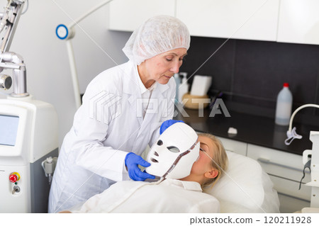 Elderly cosmetologist performing anti-aging face phototherapy procedure Elderly cosmetologist performing anti-aging face phototherapy procedure 120211928