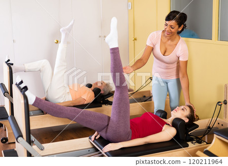 Female trainer controlling young woman doing pilates on reformer 120211964