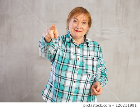 Positive elderly woman in plaid shirt pointing towards with hand Positive elderly woman in plaid shirt pointing towards with hand 120211991