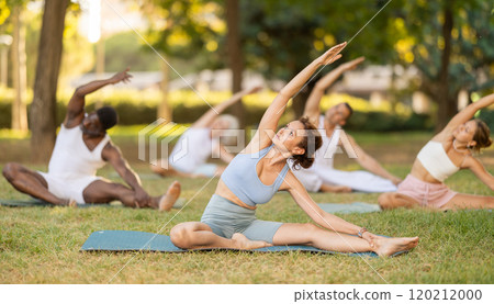Woman performing Parivrtta Janu Sirsasana during group yoga class in park Woman performing Parivrtta Janu Sirsasana during group yoga class in park 120212000