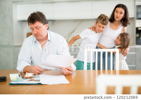 Frustrated husband is sitting in kitchen and carefully reading loan agreement. 120212069