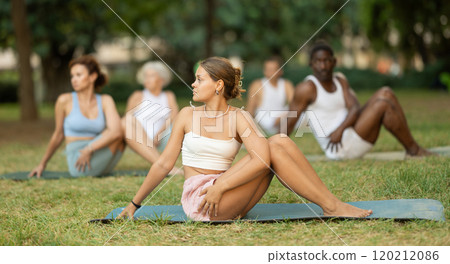 Girl performing Vakrasana during group yoga session outdoors 120212086
