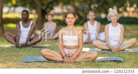 Smiling girl performing butterfly pose during group yoga in park Smiling girl performing butterfly pose during group yoga in park 120212335