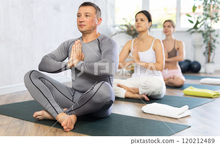 Man meditating in lotus position with hands in namaste in yoga studio 120212489