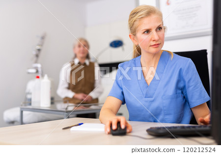 Female cosmetologist using computer while patient waiting 120212524