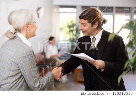 Smiling businessman with papers shaking hands with elderly woman 120212583