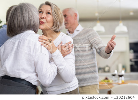 After chatting and gatherings, two mature women friends hug and kiss goodbye. 120212604