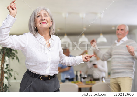 Party people celebrating friendship. Four mature friends dancing and singing at home. Cheerful women and men enjoy music together 120212609