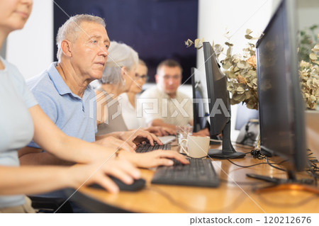 Focused older gentleman using computer at internet cafe 120212676