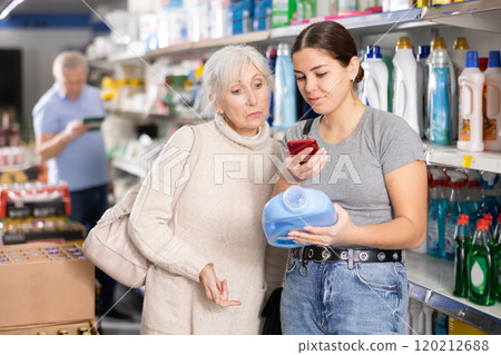Young and mature woman shopping in supermarket, chooses plastic bottle of household detergent 120212688