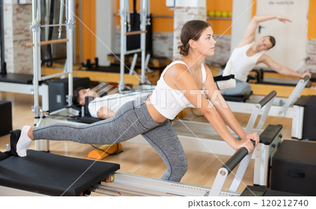 Girl performing exercises on Pilates reformer in fitness studio Girl performing exercises on Pilates reformer in fitness studio 120212740