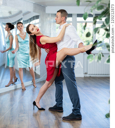 Couple in stage costumes learns tango dancing during individual lesson 120212873
