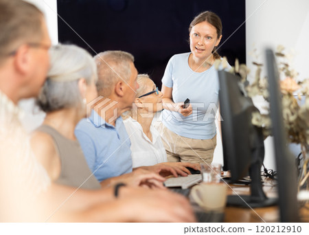 Middle-aged woman teacher speaking to mature attendees of computer courses 120212910