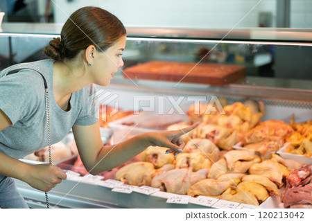 Young woman buyer chooses chicken in butcher shop 120213042