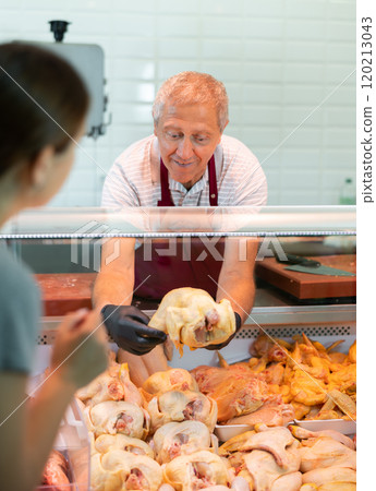 Senior male seller offers girl to buy fresh dressed chicken. 120213043