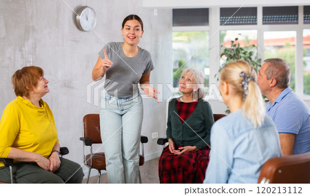 Young female tutor communicating with elderly people in language club 120213112