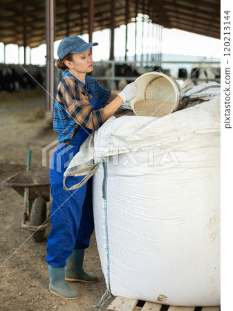 Woman in overalls pours dry feed for cows into a bucket. Work on farm Woman in overalls pours dry feed for cows into a bucket. Work on farm 120213144