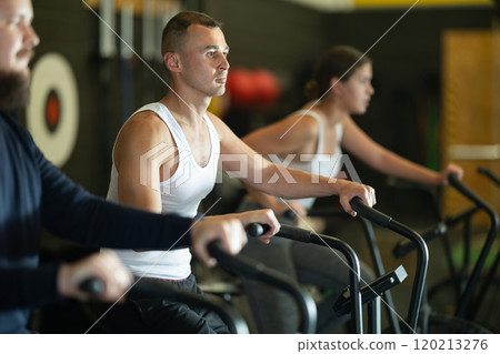 Sportive young guy doing air bike exercises in well-equipped gym 120213276