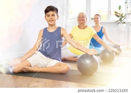 Family grandmother, mother and grandson perform fitness exercise sitting on floor with softball 120213285