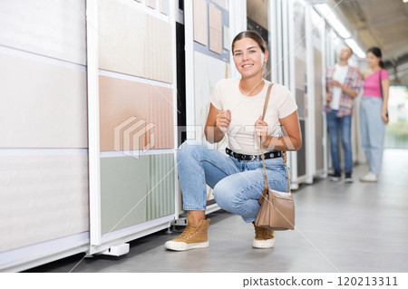 Girl in a hardware store choosing floor ceramic tiles for his apartment 120213311