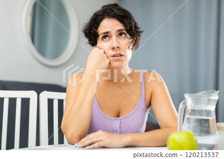 Portrait of thoughtful girl sitting at table in apartment 120213537