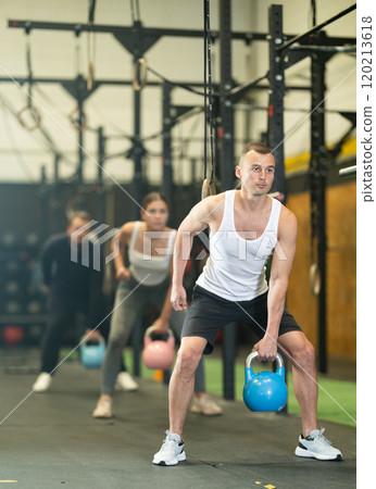Sportive young man lifting heavy kettlebell in sports hall 120213618