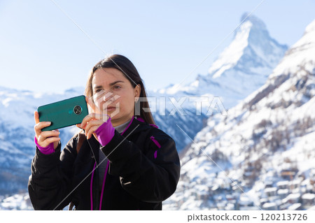 Woman recording video with phone while traveling in winter Swiss Alps Woman recording video with phone while traveling in winter Swiss Alps 120213726