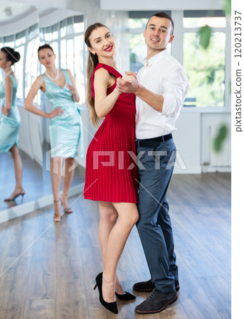 Woman in red dancing slow foxtrot with male partner in studio 120213737