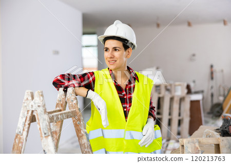 Young female civil engineer in helmet and safety vest leaning on stepladder at construction site Young female civil engineer in helmet and safety vest leaning on stepladder at construction site 120213763