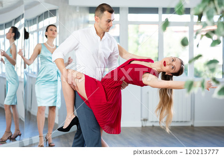 Couple in stage costumes learns tango dancing during individual lesson 120213777
