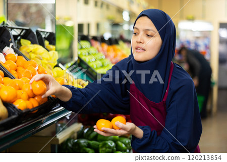 Muslim female seller in hijab chooses ripe mandarin Muslim female seller in hijab chooses ripe mandarin 120213854