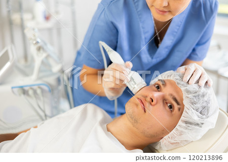 Young woman cosmetologist doing whitening procedure to young man 120213896