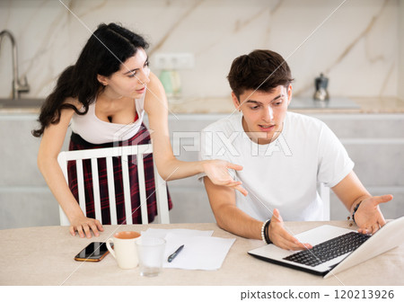 Sad freelancer husband works at home on laptop and listens to her wife reproaches in frustration. Sad freelancer husband works at home on laptop and listens to her wife reproaches in frustration. 120213926
