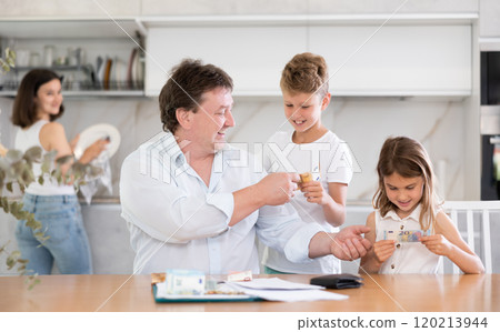 Adult man sitting at table distributes money to family Adult man sitting at table distributes money to family 120213944