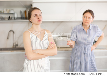 Offended young girl standing in the kitchen, angry mother talking Offended young girl standing in the kitchen, angry mother talking 120213949