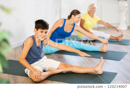 Preteen boy practicing head to knee pose of yoga in light fitness room Preteen boy practicing head to knee pose of yoga in light fitness room 120214007