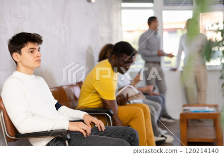 Young male visitor sitting on the bench in waiting room of clinic Young male visitor sitting on the bench in waiting room of clinic 120214140