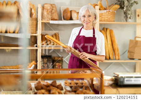 Mature woman entrepreneur, owner of baker puts baguettes in paper bag. Mature woman entrepreneur, owner of baker puts baguettes in paper bag. 120214151
