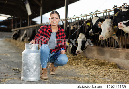 Successful girl farmer posing with milk can near stall with cows 120214189