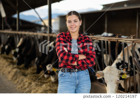 Positive young woman farmer in cowshed Positive young woman farmer in cowshed 120214197