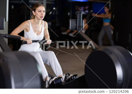 Girl performs exercises with rowing machine in gym 120214206