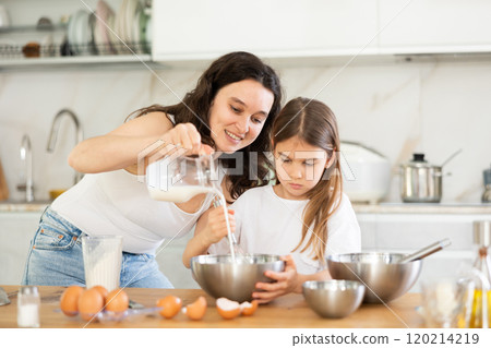 Mother and daughter adding milk in metal bowl in the kitchen 120214219