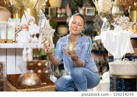 Happy middle-aged female consumer choosing Christmas decorations in decorated hall 120214259