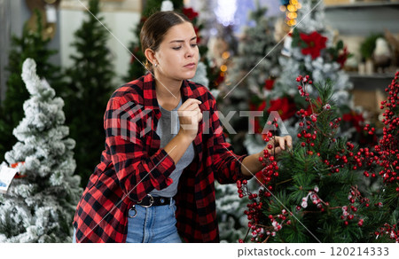 Excited young female choosing an artificial Christmas tree decorated with viburnum at the December 120214333