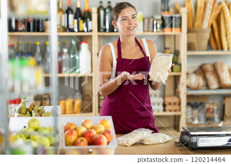 Young woman seller offering oat flakes in grocery store Young woman seller offering oat flakes in grocery store 120214464