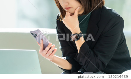 A woman/businesswoman thinking seriously while using a computer and smartphone A woman/businesswoman thinking seriously while using a computer and smartphone 120214489
